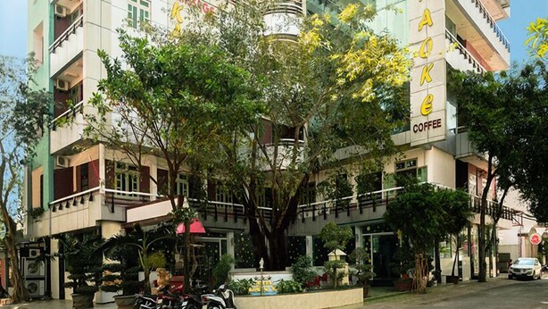A multi-story hotel with balconies, a coffee shop on the ground floor, and a central courtyard with trees. - Tuan Vu Hotel (Buon Ma Thuot)