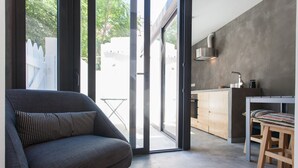 Un espai de vida modern amb un sofà gris, un tamboret de fusta i una zona de cuina amb un rentapeus i els armaris.