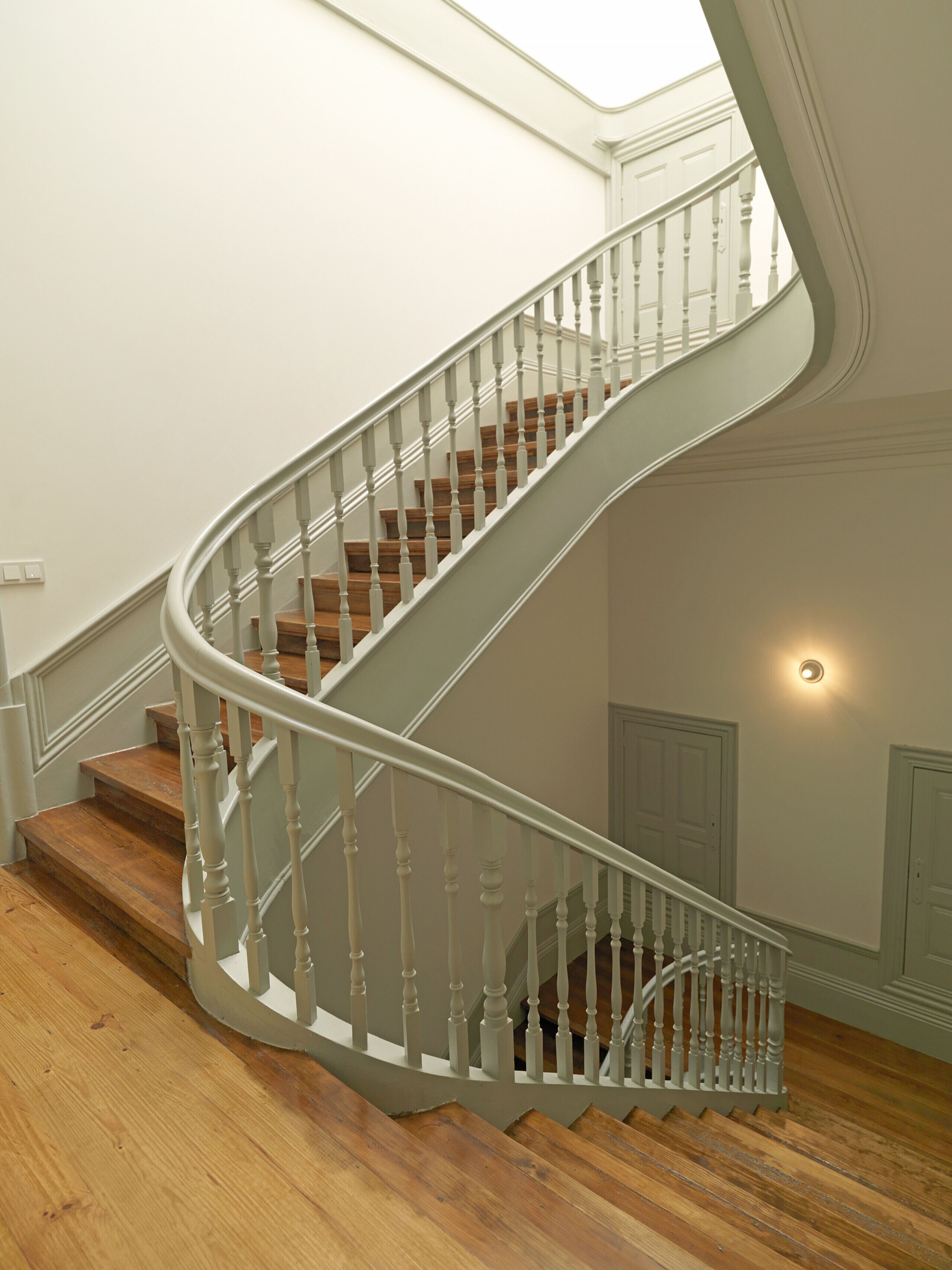 Eine Wendeltreppe mit Holzbodenstufen und weißen Geländern, die zu einer oberen Etage führt.
