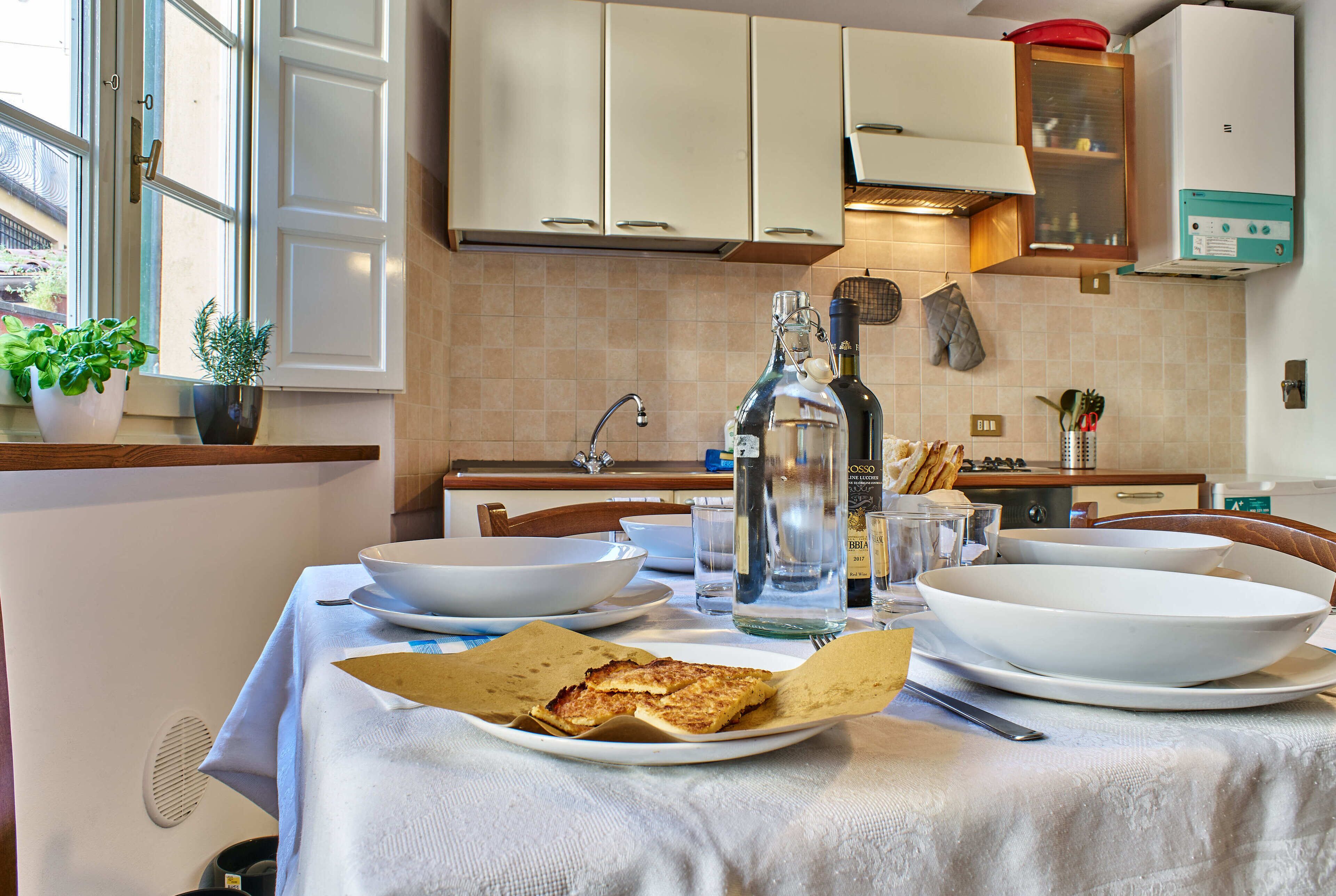 A kitchen with white cabinets, a stove, and a dining table set with plates, bowls, and a bottle.