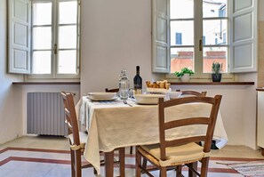 A dining area with a table set for two, a radiator, and a window with a view of buildings. - Bilocale Torre Guinigi (Lucca)