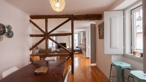 A dining area with a wooden table and chairs, a chandelier, and a view of the living room through an open door.