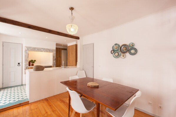 Un coin repas avec une table en bois, des chaises blanches, un lustre et des assiettes décoratives accrochées au mur.