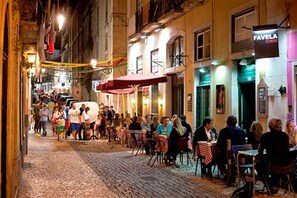 Une rue pavée bordée de cafés et de restaurants en plein air, où l’on peut voir des gens dîner et se promener.