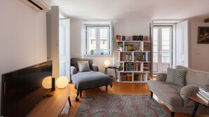 A living room with a flat-screen TV, a sofa, a chair, a bookshelf, and a window.