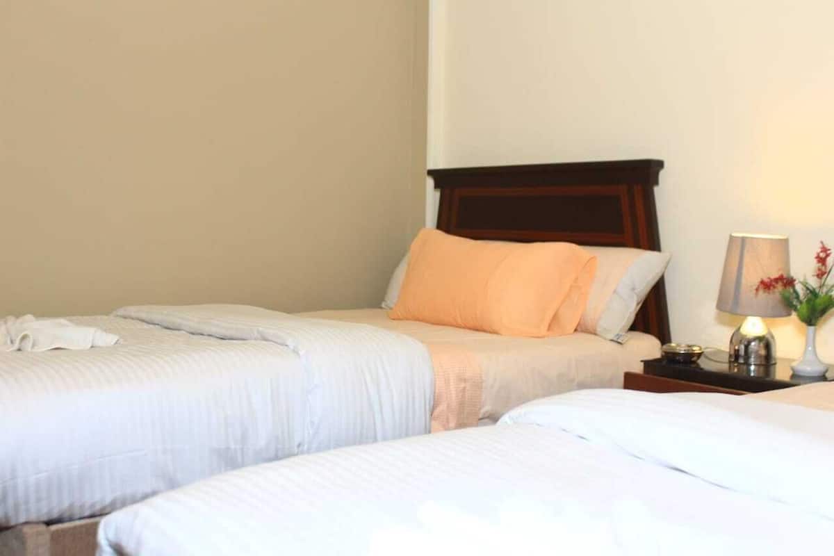 A hotel room with two beds, a wooden headboard, a bedside table with a lamp, and a vase with flowers.
