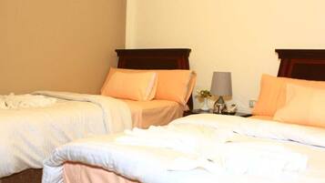 Dos camas individuales con cabeceros a juego y ropa de cama naranja, una mesita de noche con lámpara y un teléfono fijo en la pared.