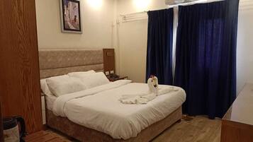 A hotel room with a bed, a nightstand, a picture on the wall, and a window with curtains.