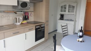 A modern kitchen with a microwave, kettle, and stove. There is a dining table with a chair and a bottle of wine. - Apartment "lake Ehmetsklinge" (Zaberfeld)