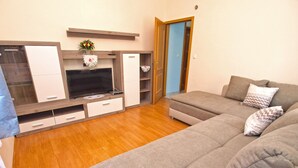 Ein modernes Wohnzimmer mit grauem Sofa, Holzboden, Flachbildfernseher und Einbauschränken.