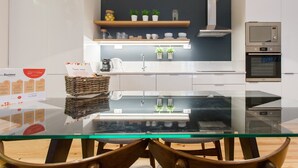 Una cocina moderna con una mesa de vidrio, sillas de madera, horno empotrado y cafetera.