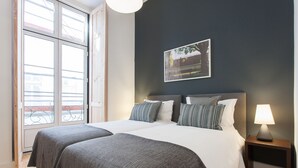 Una cama doble con ropa de cama gris, una mesita de noche con una lámpara y un cuadro en la pared.