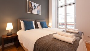 Habitación de hotel con una cama grande, dos lámparas de noche, una ventana con vistas y un cuadro enmarcado en la pared.