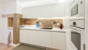 A modern kitchen with white cabinetry, a wooden accent wall, a built-in oven, and a microwave. - FLH Santa Marta Portuguese Flat (Lisbon)