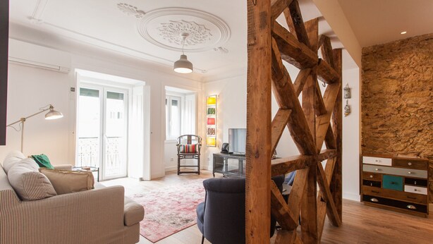 A spacious living room with a wooden beam structure, a sofa, a chair, and a desk with a computer. - FLH Santa Marta Portuguese Flat (Lisbon)