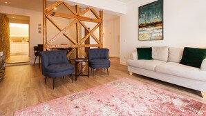 A modern living room with a wooden accent wall, two blue armchairs, a white sofa with green cushions, and a large abstract painting. - FLH Santa Marta Portuguese Flat (Lisbon)