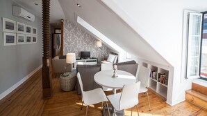 Um espaço de estar moderno estilo loft, com área de jantar, sofás, televisão e estante.