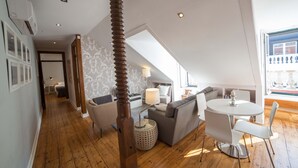 Um loft moderno com pé-direito alto, piso de madeira, área de jantar com mesa e cadeiras redondas, sofá e uma grande janela com vista.