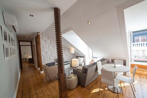 A modern loft with a high ceiling, wooden flooring, a dining area with a round table and chairs, a sofa, and a large window offering a view. - FLH Chiado Terrace Flat (Lisbon)