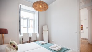 A bedroom with a bed, a desk, and a chair. There is a window with a view of buildings outside. - FLH Baixa Modern Place (Lisbon)