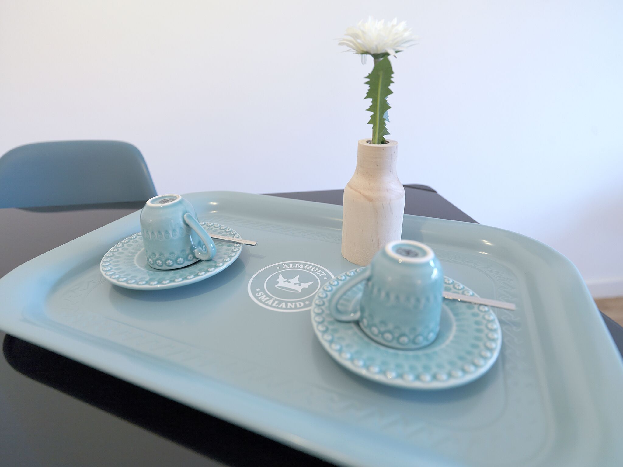 A tray with two blue cups and saucers, a white vase with a white flower, and a wooden bottle.