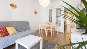 A modern living room with a grey sofa, a white coffee table, and a dining area with wooden chairs and a white table. - FLH Marquês Bright Apartment (Lisbon)