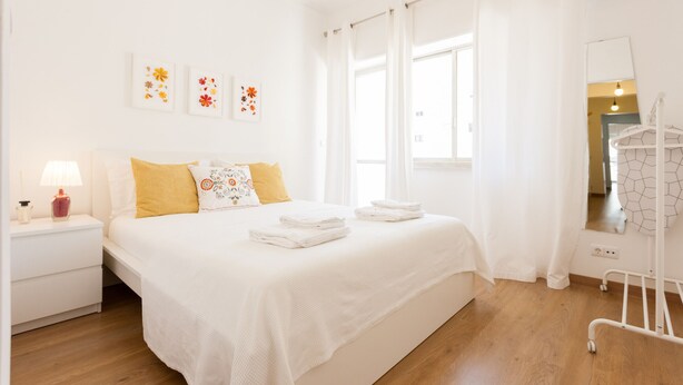 A neatly arranged bedroom with a bed, bedside table, and a hanging rack. - FLH Marquês Bright Apartment (Lisbon)