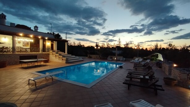 Une piscine dotée d’une terrasse en pierre, de chaises longues et d’un espace salon couvert agrémenté de luminaires.