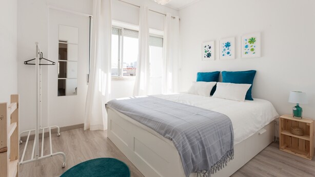 Un dormitorio con cama, mesita de noche, lámpara colgante, armario y ventana con cortinas.