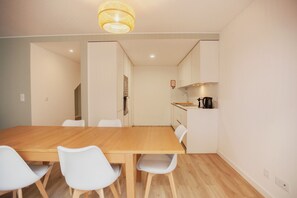 A modern kitchen with a wooden table and white chairs, a hanging light fixture, and a small island with a coffee machine. - FLH Salitre Modern Garden Apartment (Lisbon)