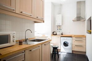 A modern kitchen with wooden cabinets, a built-in microwave, a sink, a washing machine, and a stainless steel range hood.