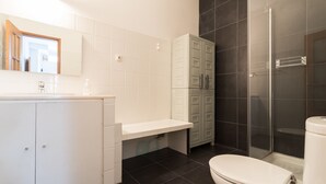 Moderni kylpyhuone, jossa on valkoinen pesuallas, peili, wc ja suihkutila.