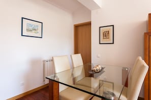 Un coin repas avec une table en verre et quatre chaises, un radiateur et deux tableaux encadrés accrochés aux murs.