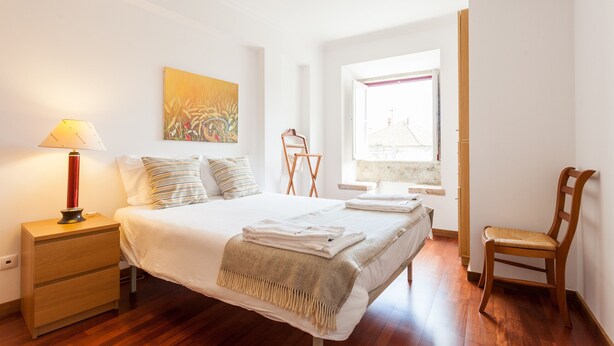 A neatly arranged bedroom with a bed, bedside lamp, and a window with a view. - FLH Olivais Cozy Flat (Lisbon)
