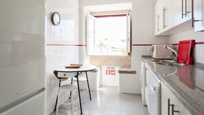 A modern kitchen with white cabinetry, a built-in oven, a sink, and a window with a view. - FLH Olivais Cozy Flat (Lisbon)