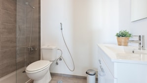 Un baño moderno con cabina de ducha de vidrio, inodoro y lavamanos con una planta en la encimera.