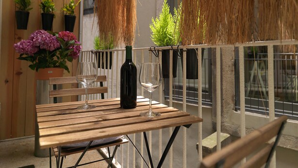 A wooden table with a wine bottle and glass, surrounded by potted plants and a railing. - FLH Porto Stylish Apartment (Oporto)