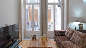 A living room with a sofa, a coffee table, a TV, and a balcony with a view. - FLH Porto Stylish Apartment (Oporto)