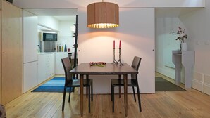 A modern dining area with a wooden table, four chairs, and a hanging pendant light. A kitchen is visible in the background. - FLH Porto Stylish Apartment (Oporto)
