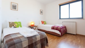 A room with two beds, a window, a radiator, and a lamp.
