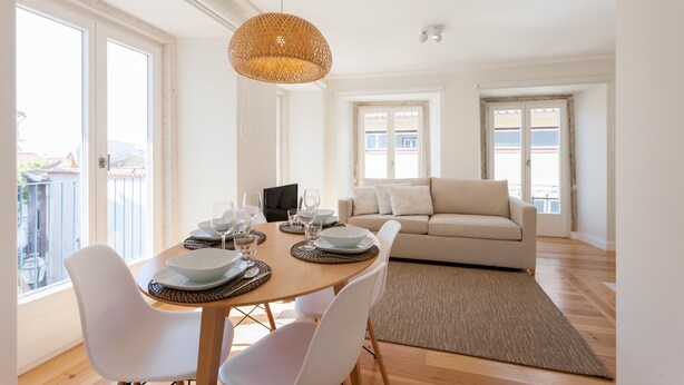 Een eetruimte met een houten tafel gedekt voor vier personen, witte stoelen en een geweven hanglamp.