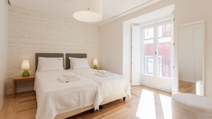 Een slaapkamer met twee bedden, een houten vloer, een witte muur met een reliëfpatroon en een deur naar een buitenbalkon.