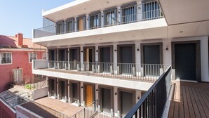 A modern multi-story building with balconies, a wooden deck, and a red building in the background. - FLH Amazing Bairro Alto Flat (Lisbon)