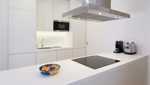 A modern kitchen with white cabinetry, a built-in microwave, a stainless steel range hood, a black induction cooktop, and a coffee maker. - FLH Amazing Bairro Alto Flat (Lisbon)