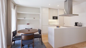 A modern kitchen with white cabinetry, a round dining table with chairs, and a built-in island with a sink and appliances. - FLH Amazing Bairro Alto Flat (Lisbon)