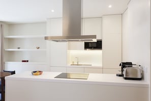 A modern kitchen with white cabinetry, a stainless steel range hood, a built-in microwave, a toaster, and a bowl on the counter.