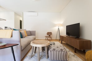 A modern living room with a sofa, a round wooden table, a television on a wooden cabinet, and a floor lamp.