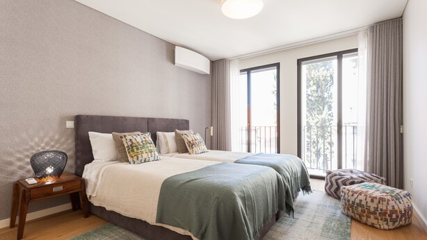 A bedroom with two beds, a nightstand, a large window with curtains, and a balcony. - FLH Amazing Bairro Alto Flat (Lisbon)