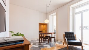 A modern living room with a wooden dining table, a black leather chair, and a hexagonal patterned rug. - FLH Bica Modern Flat with View (Lisbon)