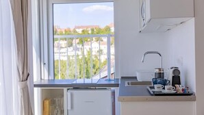 A compact kitchen with a built-in dishwasher, a small refrigerator, and a window with a balcony view. - Christina Residence (Budapest)